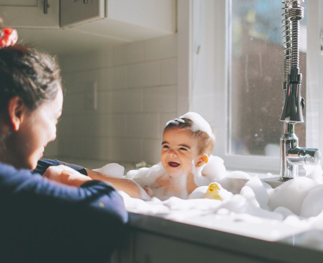 a mother smiling at her baby bathing in the sink